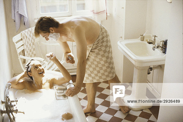 Couple together in bathroom  woman in bathtub  man leaning over her with shaving cream on face