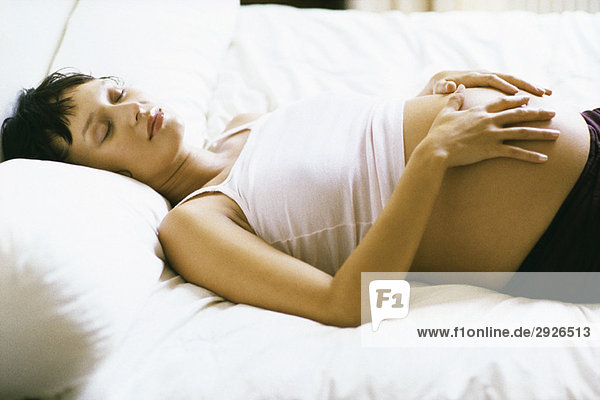 Schwangere schlafend auf dem Bett  Hände auf dem Bauch