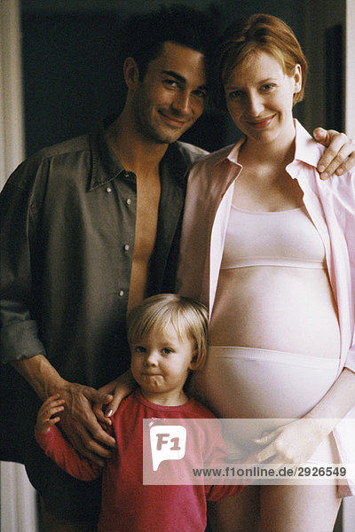 Schwangere Frau stehend mit Mann und Tochter  lächelnd vor der Kamera