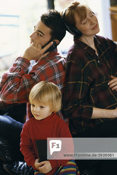 Familie sitzt Rücken an Rücken  Vater benutzt Handy  Mutter hört Kopfhörer  Tochter schaut TV
