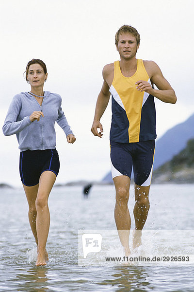 Junges Paar läuft gemeinsam durch flaches Wasser in Ufernähe