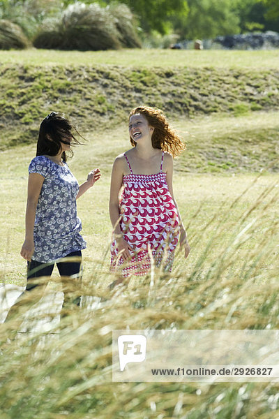 Zwei junge Frauen  die gemeinsam im Freien spazieren gehen und lachen.