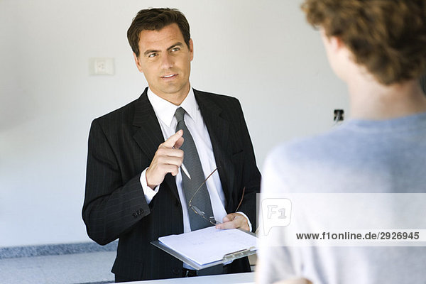 Businessman holding clipboard speaking to associate