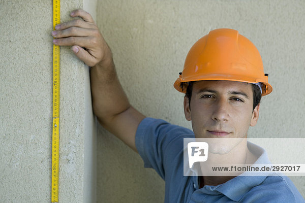 Bauarbeiter hält das Lineal an die Wand  schaut in die Kamera