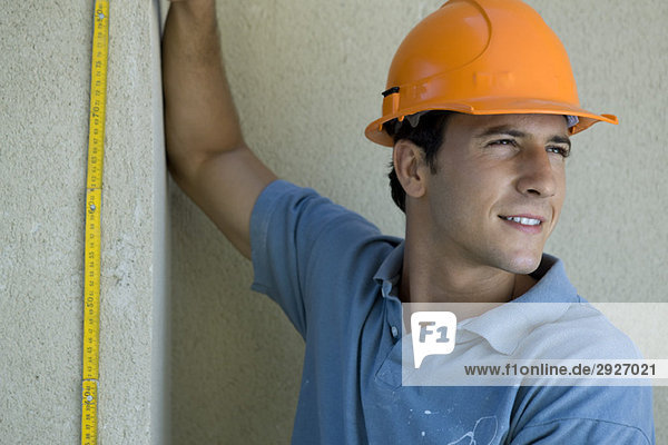 Bauarbeiter hält Lineal an der Wand  schaut weg