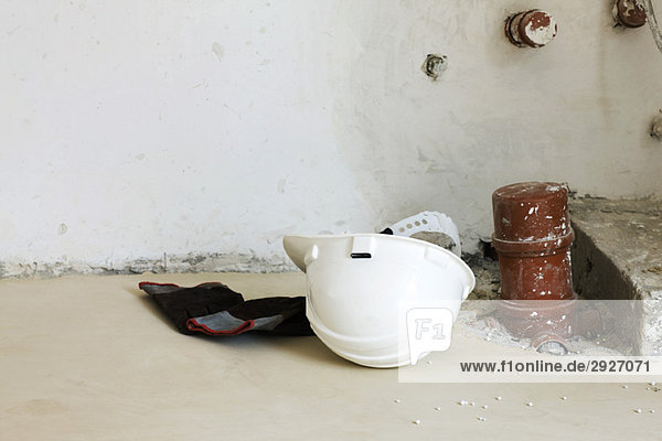 Handschuhe  Schutzhelm auf dem Boden in der Nähe der Sanitärarmatur