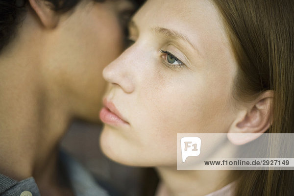 Young woman looking away distantly as man kisses her cheek