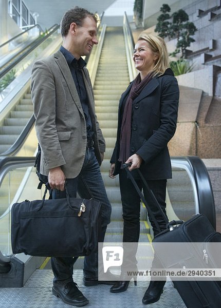 Mann und Frau mit Koffer vor der Rolltreppe