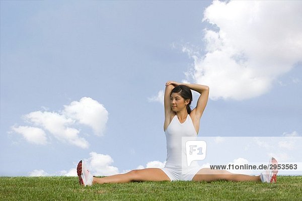 Young Woman Stretching Schultern beim Sitzen auf Gras