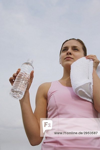 junge Frau hält Wasserflasche und abwischen Gesicht mit Handtuch