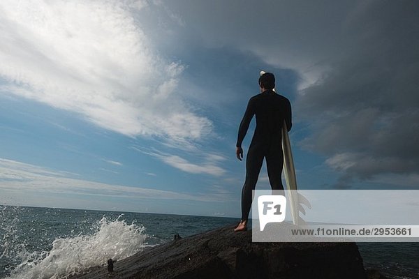 Man standing on Rock mit Surfboard Blick auf Meer