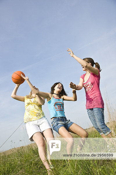 Drei junge Mädchen spielen auf Wiese mit Ball  Flachwinkelansicht