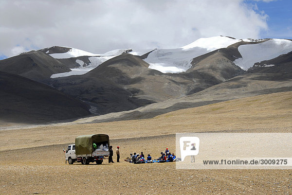 Trekking group rests near a truck below snow-capped mountains on Nam-La Pass 5250 m Everest region Tibet China