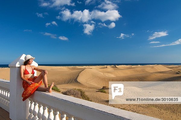 Frau sitzt auf einem Zaun und blickt auf die Sanddünen  Maspalomas  Gran Canaria  Spanien