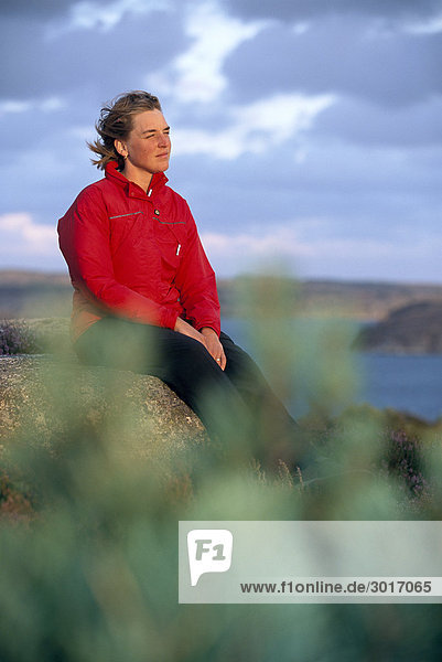 Eine Frau sitzend auf einem Felsen in den Schären.