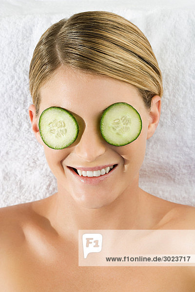 Smiling young woman lying on towel with cucumber slices over eyes
