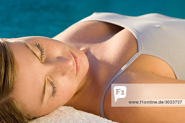Young woman lying on massage table by the pool