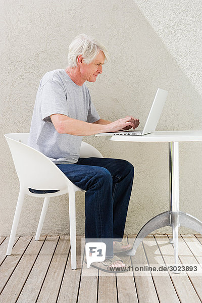 Middle aged man sitting on desk and using laptop