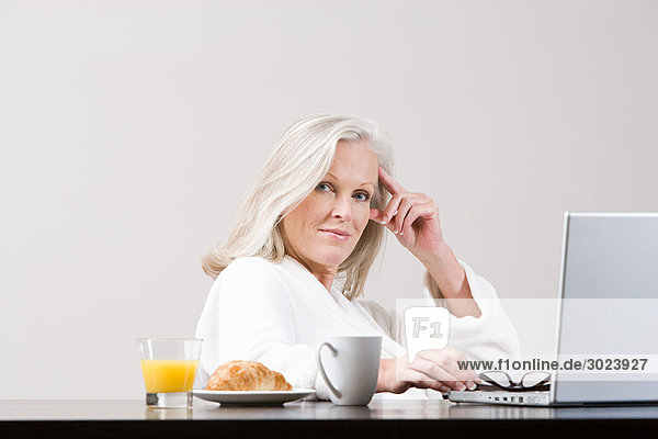 Middle aged woman using laptop at breakfast time