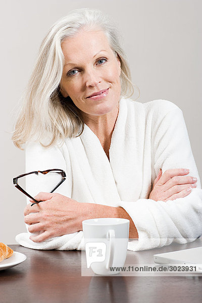 Middle aged woman sitting at breakfast table in bathrobe