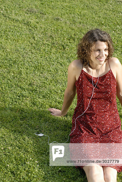 Junge Frau auf dem Rasen sitzend  MP3-Player hörend  lächelnd