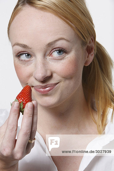 Junge Frau hält Erdbeere  lächelnd  Portrait