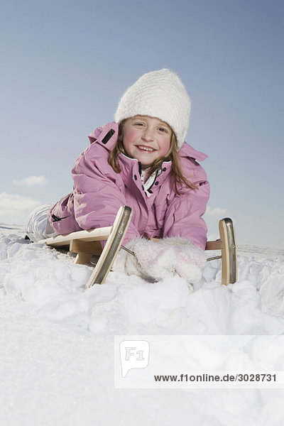 Girl (6-7) lying on sledge  smiling  portrait
