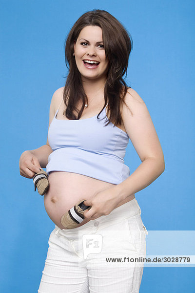 Schwangere Frau mit Babyschuhen  lächelnd  Portrait