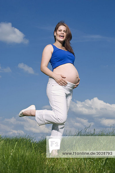 Pregnant woman standing in meadow  smiling  portrait