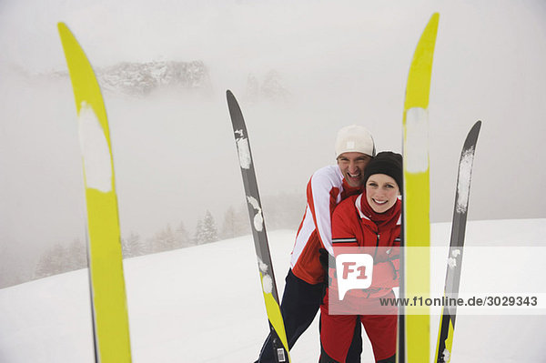 Italien  Südtirol  Paar in winte r Kleidung  lächelnd  Skier im Vordergrund