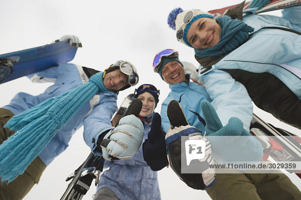 Italy  South Tyrol  Four people in winter clothes  thumbs up  low angle view