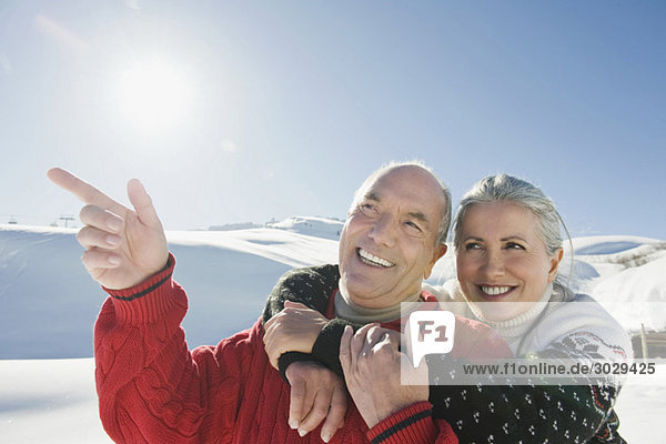 Italien  Südtirol  Seiseralm  Seniorenpaar in Winterlandschaft  Mann zeigt  Portrait  Nahaufnahme