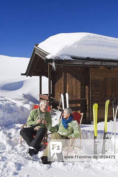 Italien  Südtirol  Seiseralm  Seniorenpaar vor Blockhütte sitzend  Sektgläser haltend