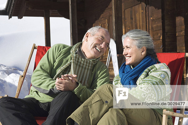 Italien  Südtirol  Seiseralm  Seniorenpaar vor Blockhaus sitzend  lächelnd  Portrait