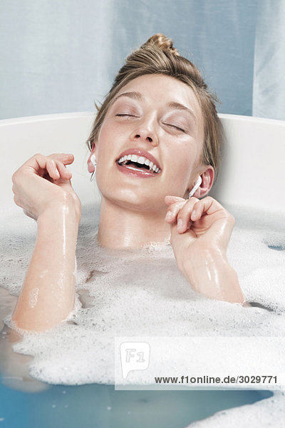 Young woman in bathtub listening to music