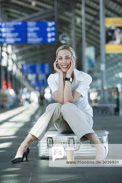 Junge Frau in der Abflughalle des Flughafens  auf dem Koffer sitzend