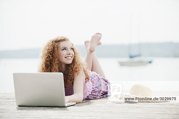 Young woman lying on jetty using laptop  portrait