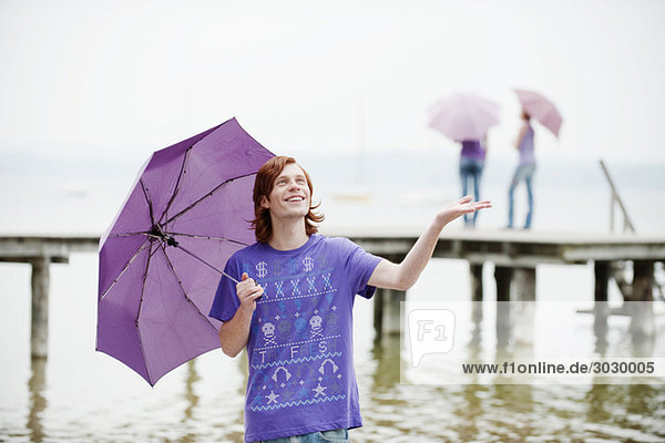 Junger Mann mit Regenschirm  Personen im Hintergrund