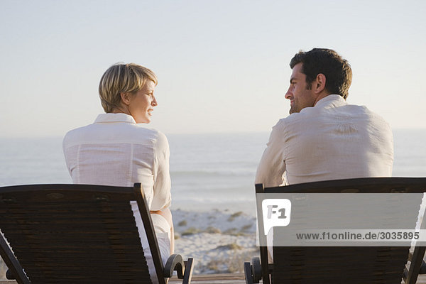 Couple sitting on deck chairs on the beach