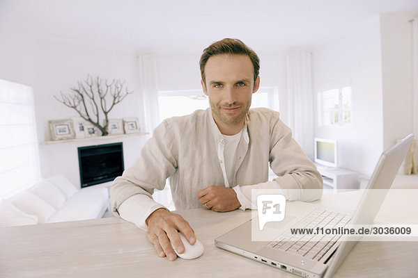 Porträt eines Mannes  der an einem Laptop arbeitet und lächelt
