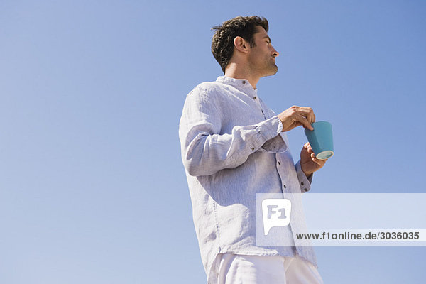 Mann mit einer Tasse Kaffee am Strand