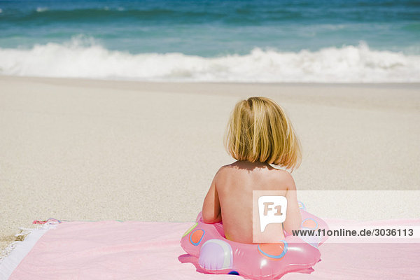 Mädchen sitzend mit aufblasbarem Ring am Strand