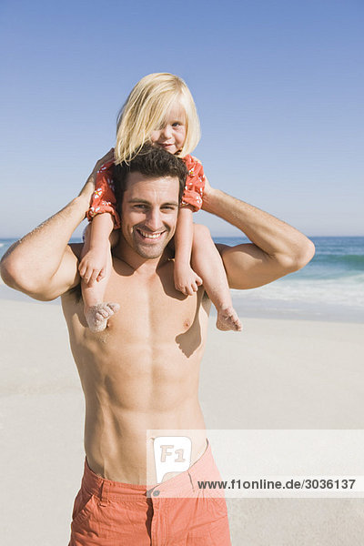 Mann mit seiner Tochter auf den Schultern am Strand