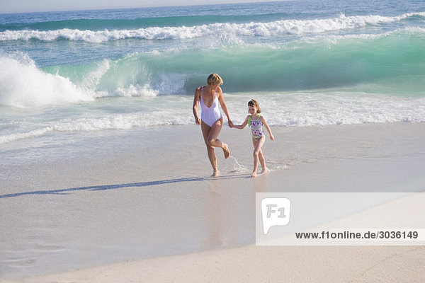 Frau  die mit ihrer Tochter am Strand rennt