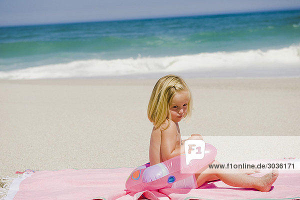Mädchen sitzend mit aufblasbarem Ring am Strand