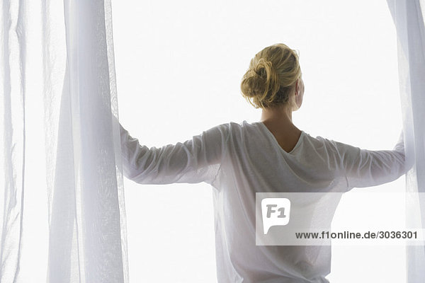 Rückansicht einer Frau beim Öffnen des Balkonvorhangs