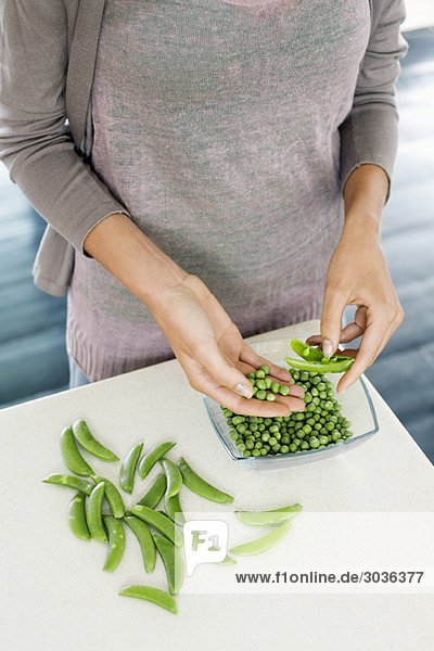 Frau schält grüne Erbsen in der Küche