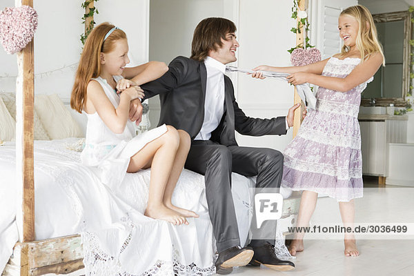 Mädchen zieht Krawatte eines Bräutigams mit einem Mädchen  das neben ihm sitzt