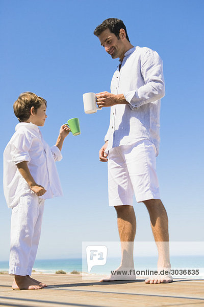 Man and his son holding coffee cups on the beach