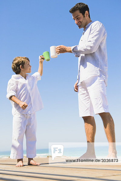 Man and his son toasting with coffee cups on the beach